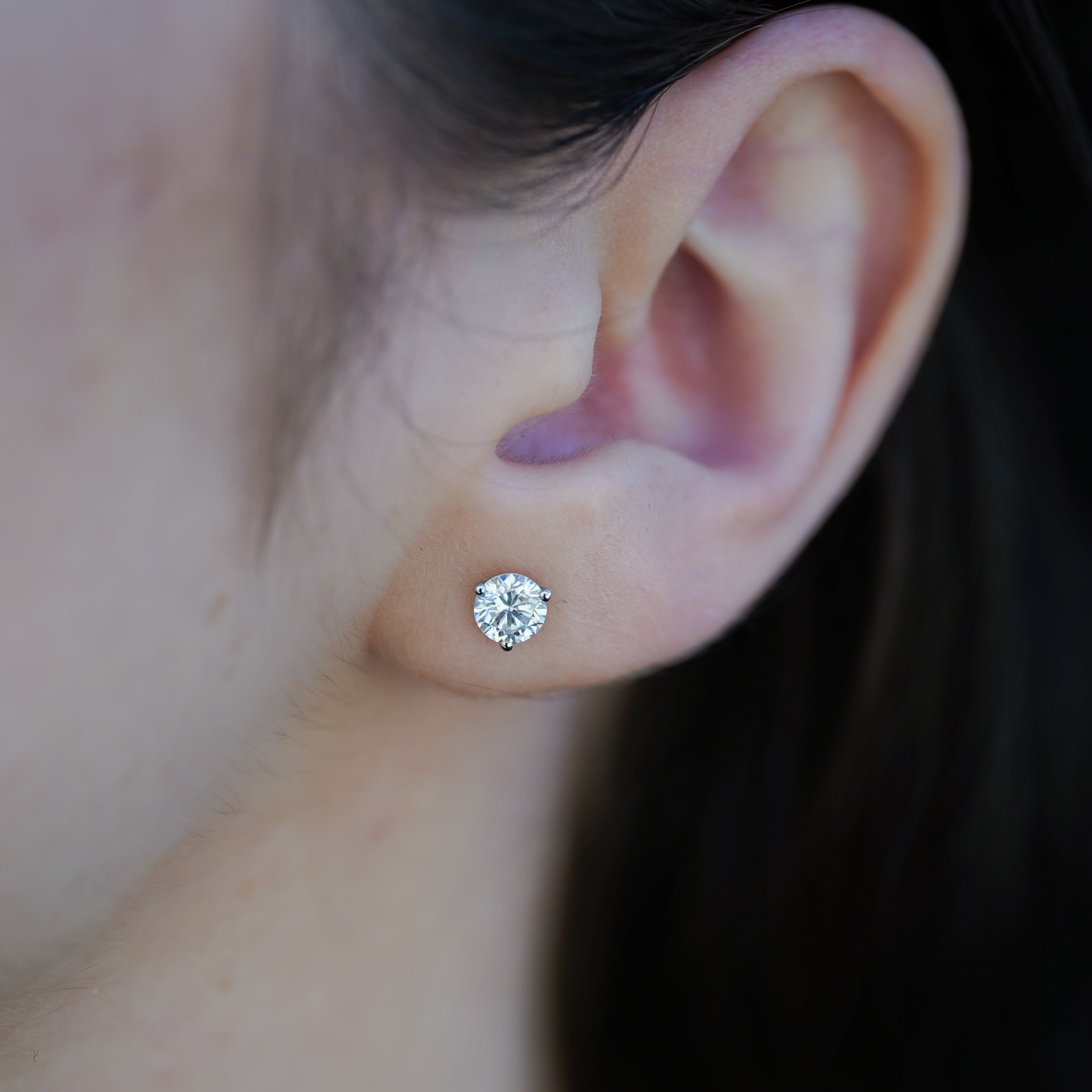 Close-up of an ear wearing a diamond stud earring with a blurred background