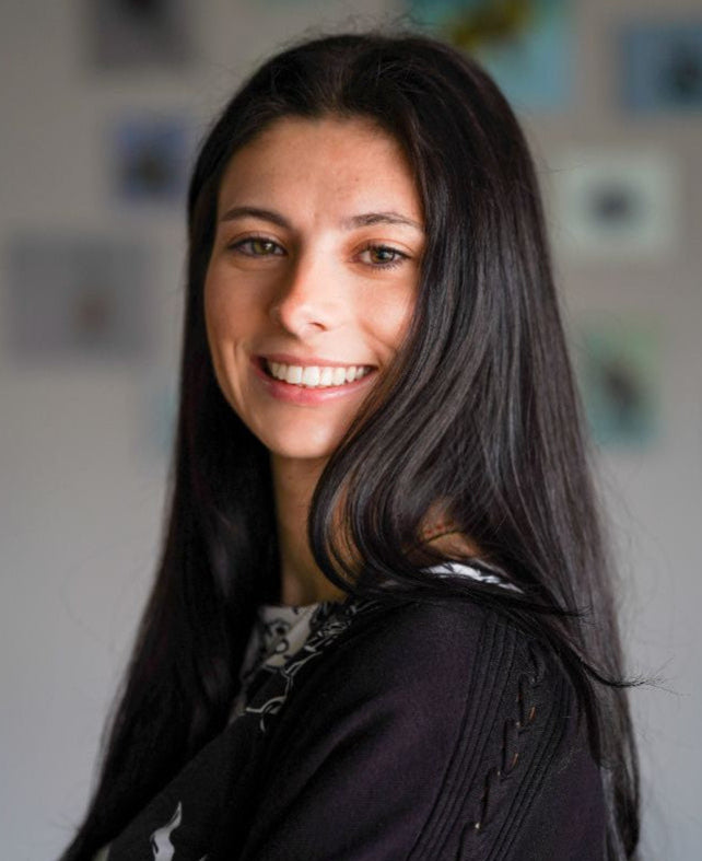 Woman with long dark hair smiling in front of a blurred background