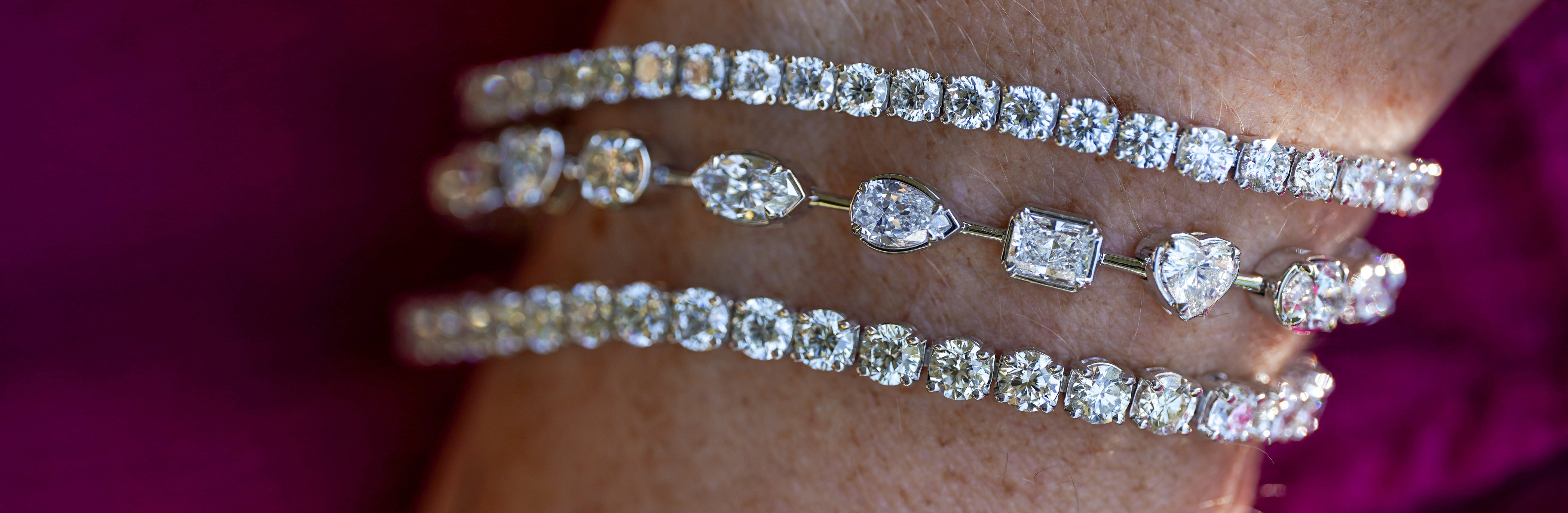 Three diamond bracelets on a person's wrist against a purple background